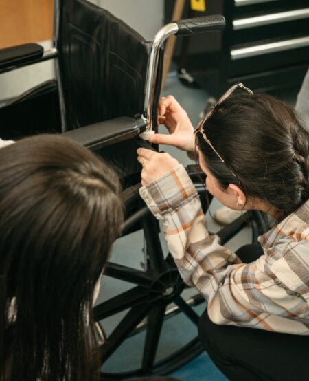 A person kneels to insert a mechanical component into a wheelchair.