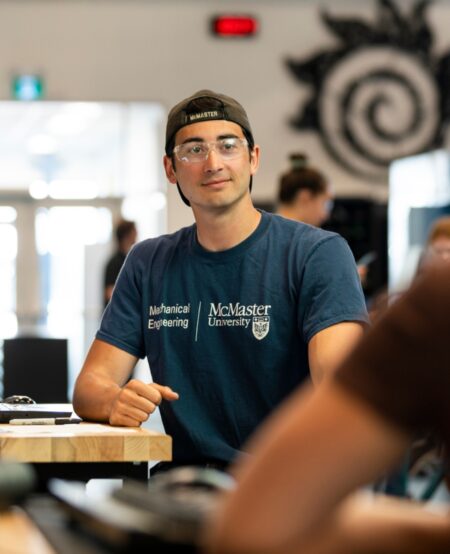 A student wearing safety glasses and a mechanical engineering shirt smiles.