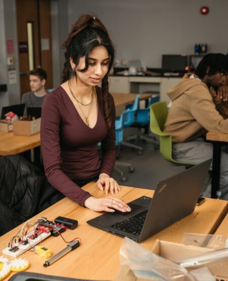 A person stands by a laptop, which rests next to electronics on a desk.