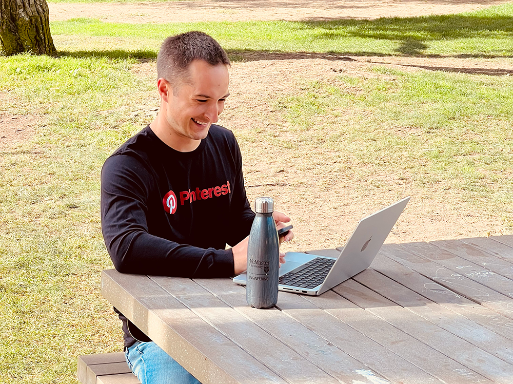 Andrew Lutz, Pinterest Front-end Software Engineer and 2011 Mechanical Engineering, sits at a table outside working on a laptop.