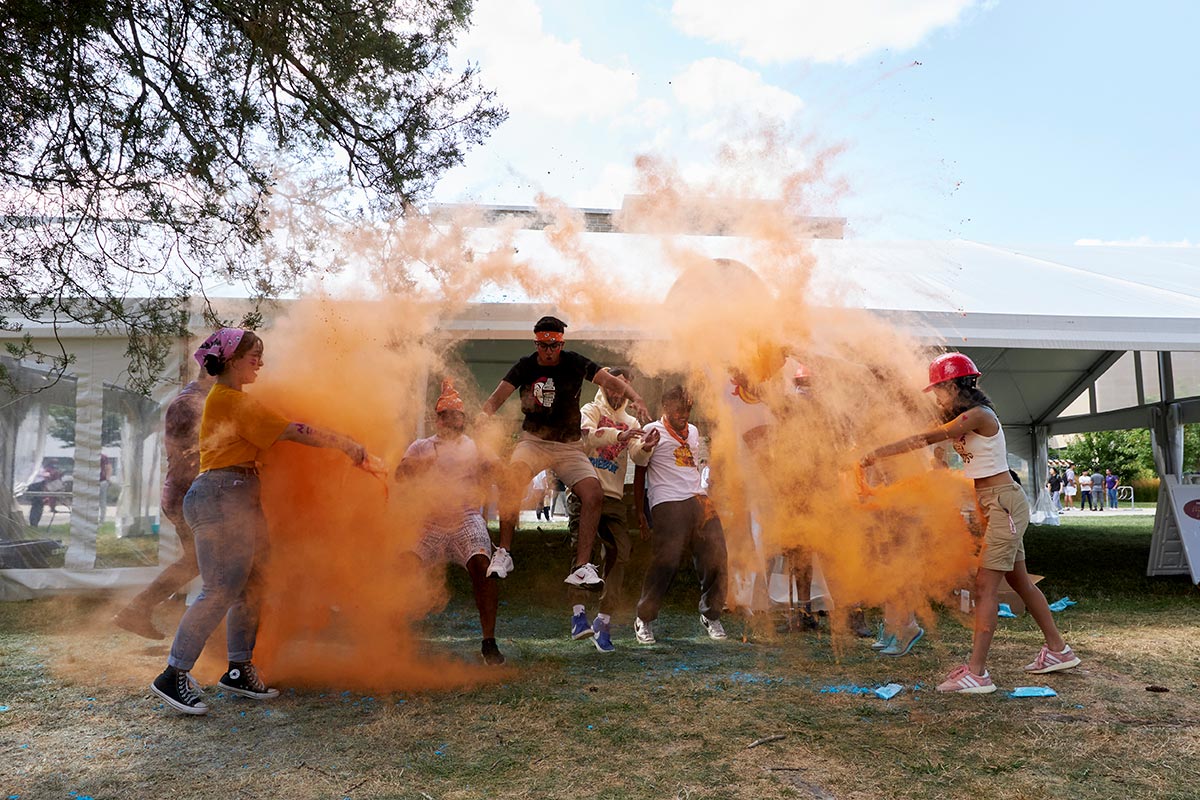 A group of students run through a cloud of orange chalk